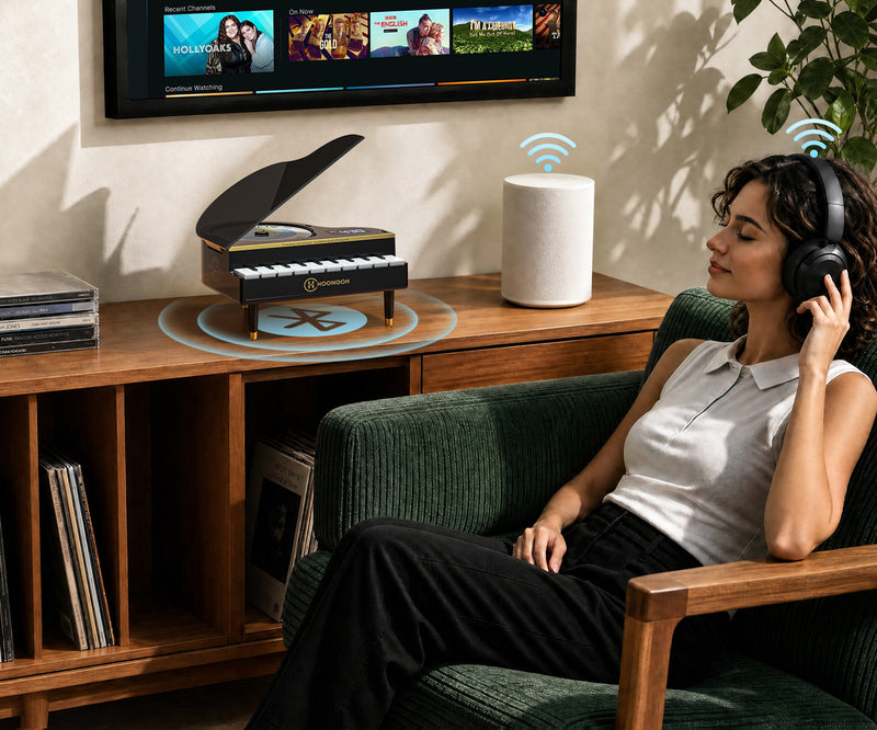 A woman relaxes in a green armchair wearing over-ear headphones, with a smart speaker and a decorative piano-shaped cd player on a wooden console in a living room setting.