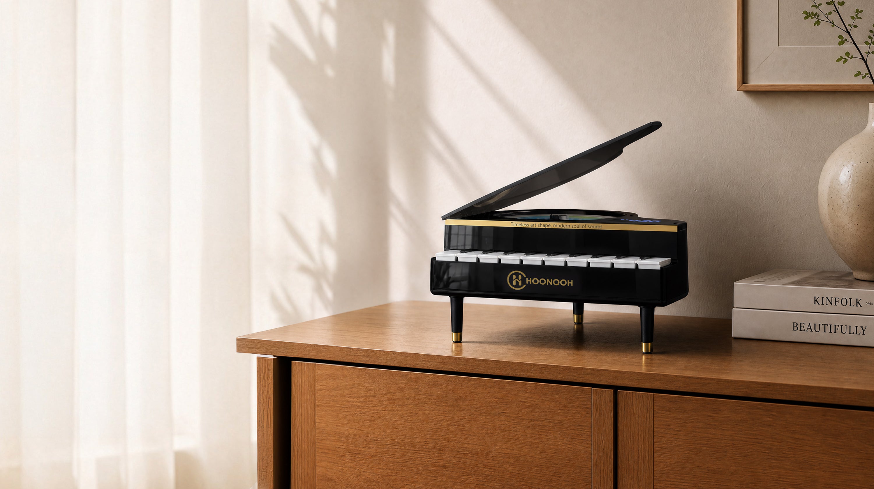 A black HONNOOPI piano-shaped cd player with gold trim and white keys sits on a wooden cabinet in a softly lit interior setting.